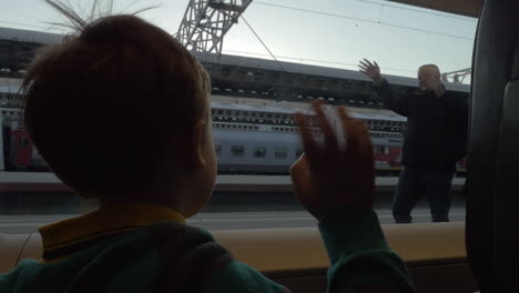 child in train waving hand to grandparents as he leaving