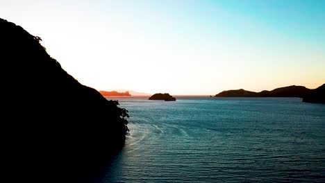 a slow pan over the ocean to reveal a gorgeous sunset as it peeks over the tops of the islands of new zealand