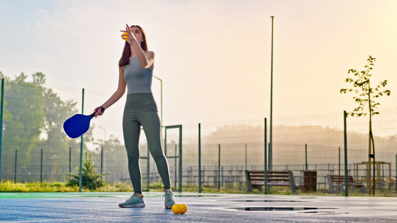 Woman playing pickleball on a blue and green court after rain
