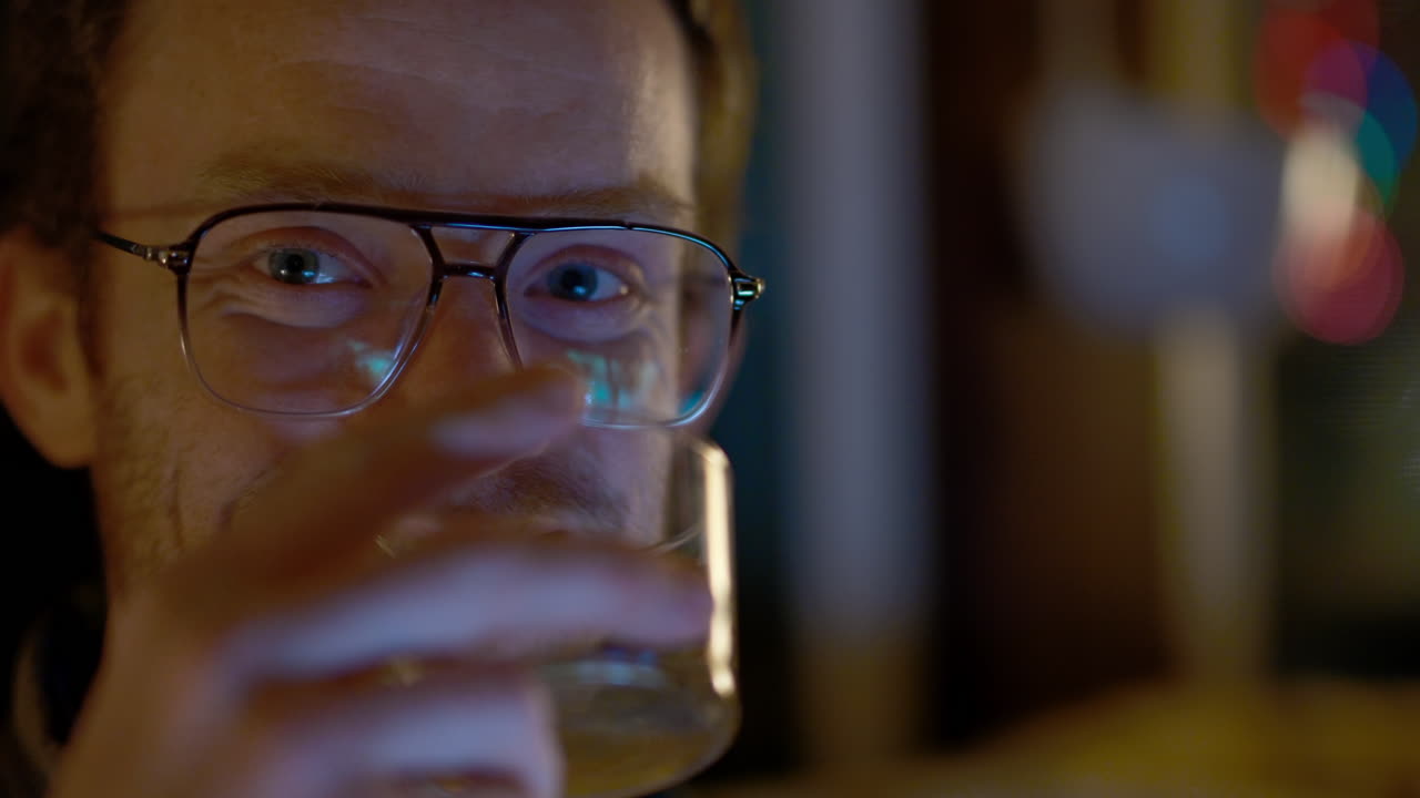 hombre con gafas mirando su teléfono y bebiendo por la noche