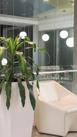 a modern indoor setting featuring potted plants positioned on either side of a glass elevator. there are two red pots, two white pots, and one brown pot with tall green plants