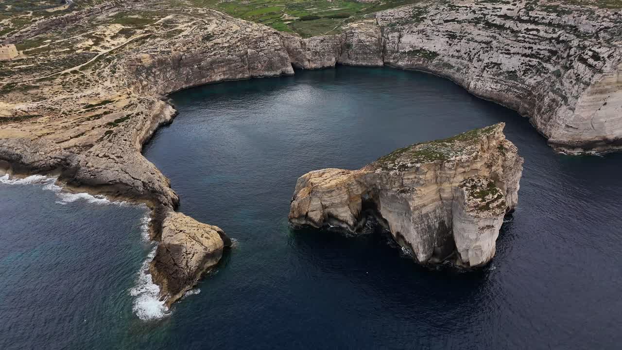 San Lawrenz Gozo Malta'daki Dwejra Koyu, İç Deniz ve Mavi Delik yakınındaki kireçtaşı deniz yatağı üzerinde turkuaz Akdeniz sularını, Alt Mercan Kireçtaşı oluşumu içinde ortaya koyuyor, yavaş drone ileri süzülüşü.