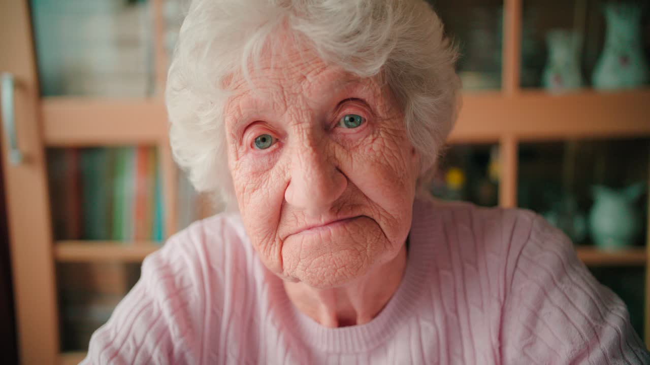 Close-up face of a sad old woman with deep wrinkles winking her eyes
