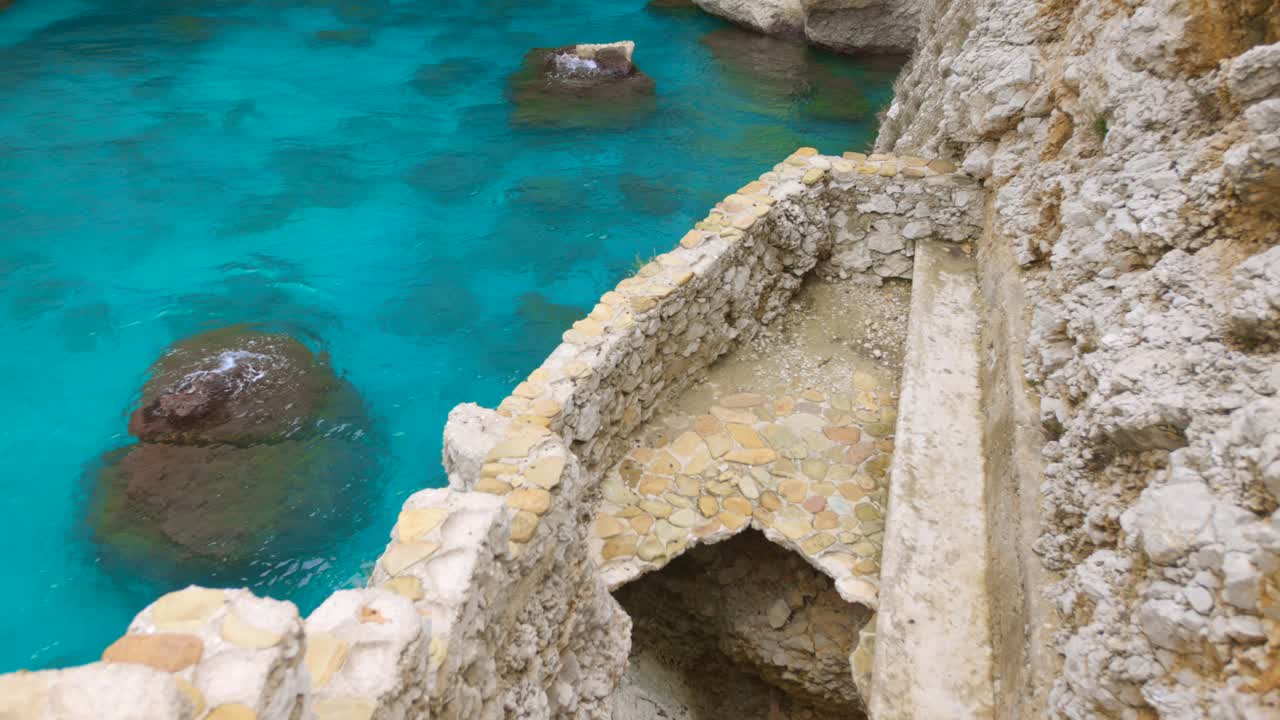 Steps made of stone guide viewers toward sparkling blue water, surrounded by rocky formations. The calm atmosphere invites exploration and relaxation in this picturesque setting.