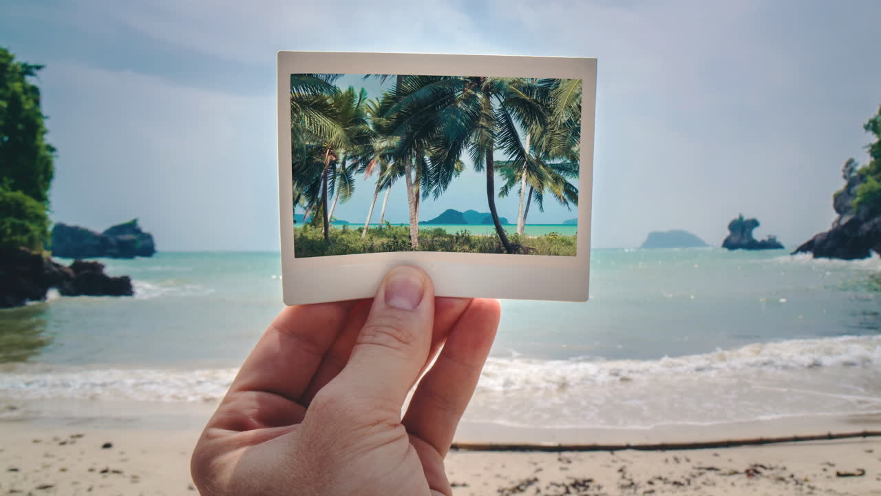 Cinemagraph of tropical Thailand beach, polaroid in hand, palm trees swaying. Static background