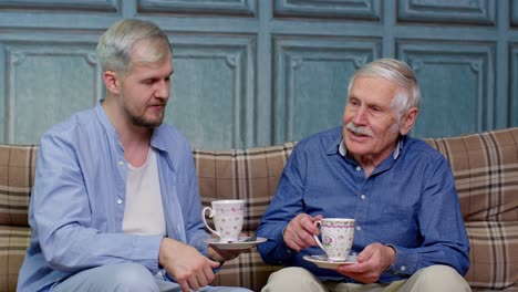 Different-male-generations-family-of-senior-father-and-adult-son-or-grandson-relaxing,-drinking-tea