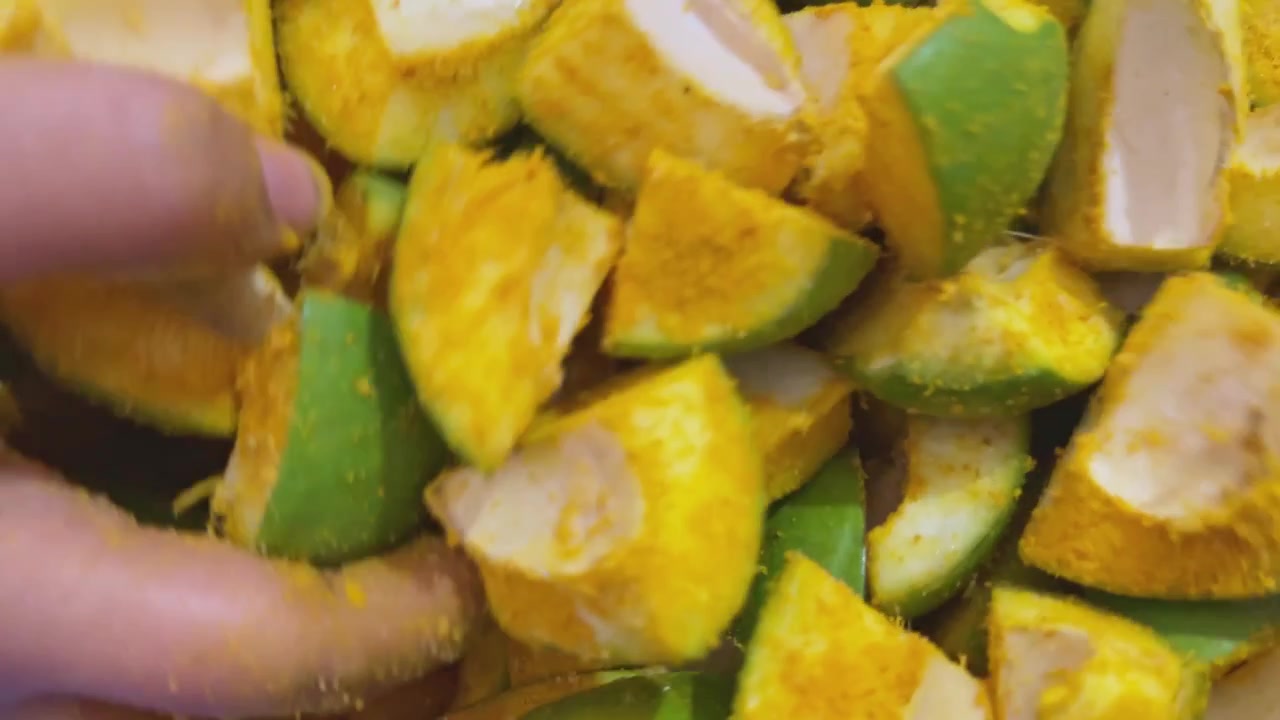 Vista ravvicinata dettagliata di pezzi di mango crudo tritati ricoperti di curcuma e sale durante il processo tradizionale di preparazione di sottaceti fatti in casa in un ambiente di cucina interna