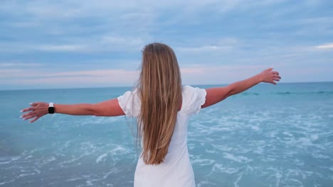 a woman joyfully standing at the beach with arms outstretched wide, savouring the serene view of the ocean