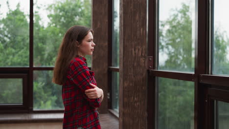 woman gazes out of window on terrace woman in checkered shirt expression reflects of weight of