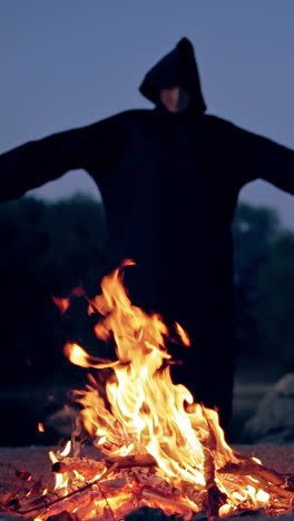 witch in black near bonfire. mystical witch walking around bonfire. vertical video