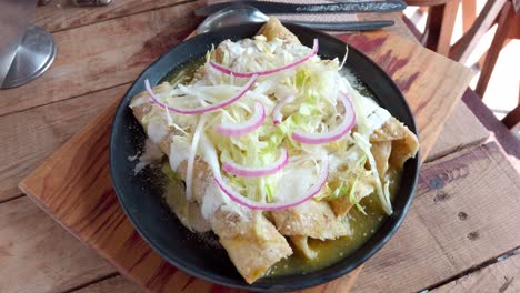 golden enchiladas with green mole, topped with lettuce and onions on rustic table
