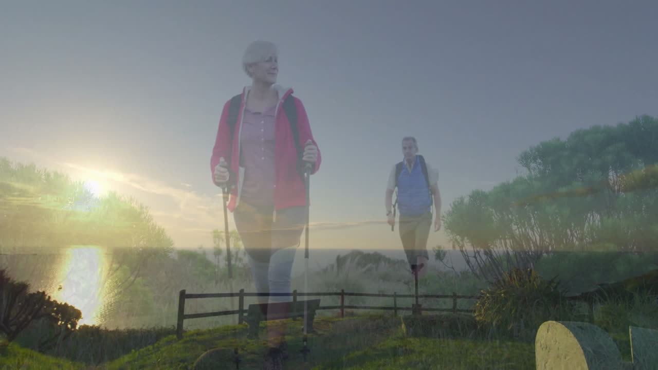 Mature couple hiking coastal travel path, woman leading with poles while man carrying backpack