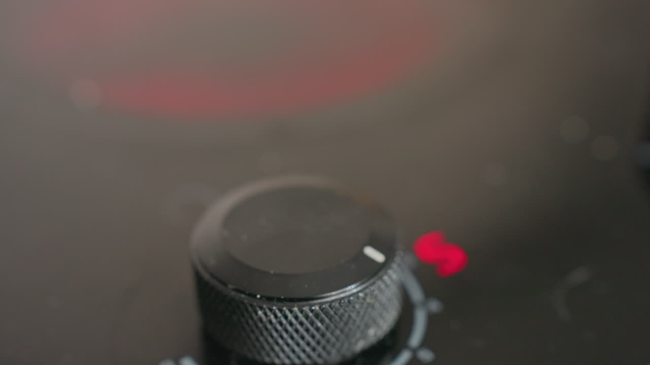 Extreme close up of fair-skinned hand adjusting electric stove knob to raise cooking temperature, focus on grip and textured black dial, showing precision in heat control
