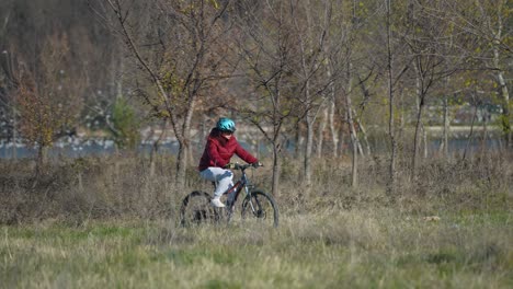 girl biking on nature shore lake with dry grass, bare trees, and white birds in background