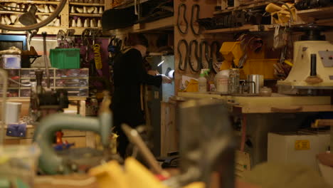 Female-shoemaker-smoothing-shoe-sole-working-on-old-fashioned-workshop-grinding-machine,-Wide-shot