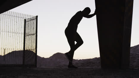 Silueta-De-Un-Hombre-Afroamericano-Enfocado-Haciendo-Ejercicio-Al-Aire-Libre,-Estirándose