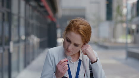 portrait attractive young red head business woman intern puts on earphones listening to music in city enjoying relaxed urban lifestyle professional caucasian female commuting