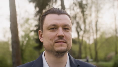 retrato de un hombre elegante mirando a la cámara y sonriendo mientras está de pie en el parque 1