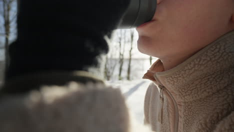 close-up of person sipping from a thermal mug on a snowy day