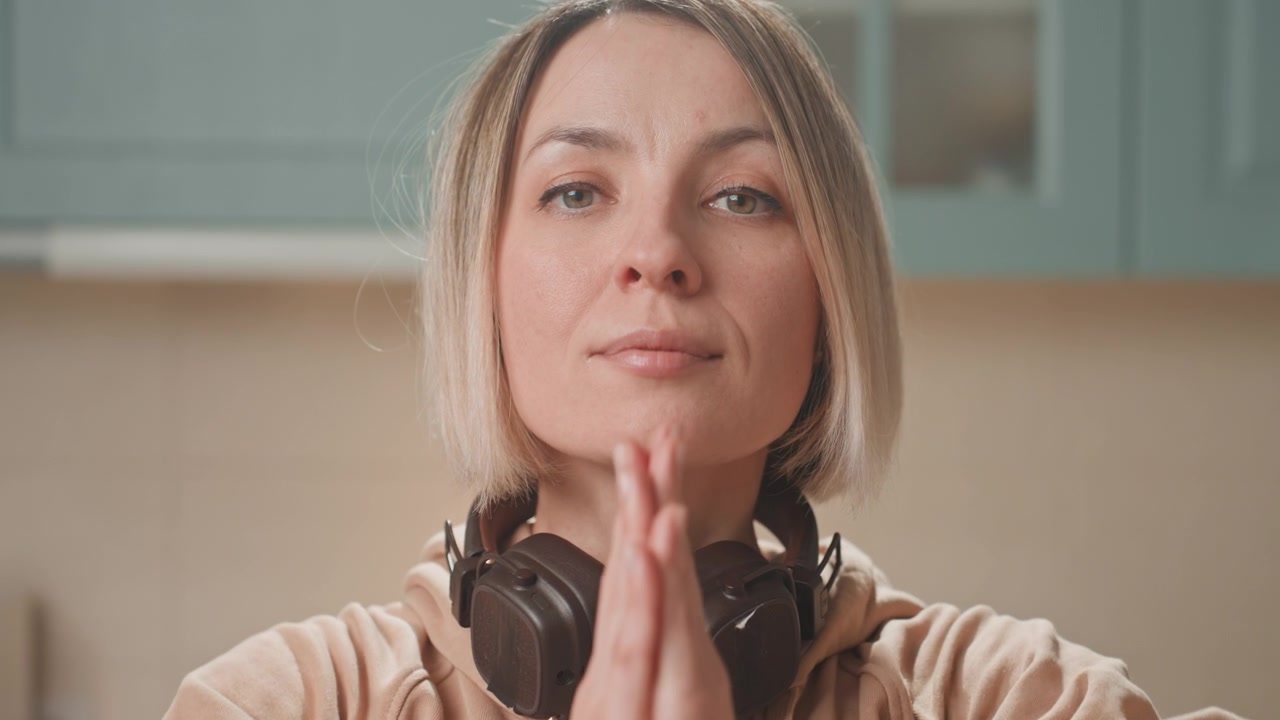 Caucasian woman in kitchen with headphones gentle barefoot stretch on rug, teal cabinets, soft morning light, headphones around neck, contemplative smile, private music lover moment
