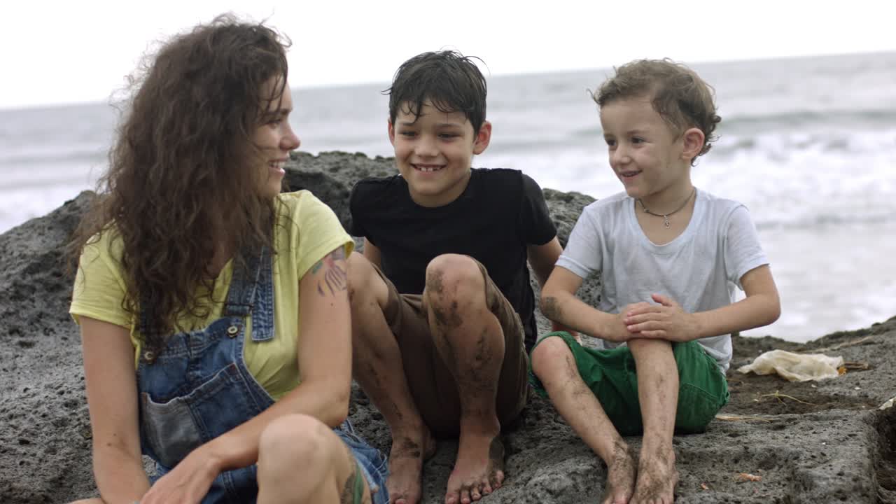 madre e hijos sentados en una piedra en la playa