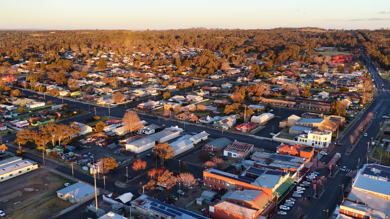 Drone glides above Coonabarabran’s main street at sunset, revealing rooftops, tree-lined avenues, and golden light over a small Australian town