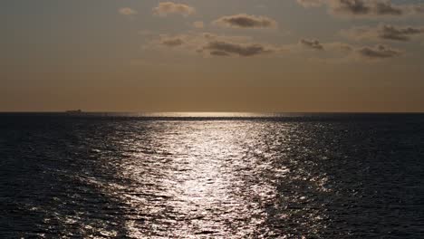 Tanker-or-container-ship-on-horizon-at-midday-under-orange-sky-and-dark-shimmering-water