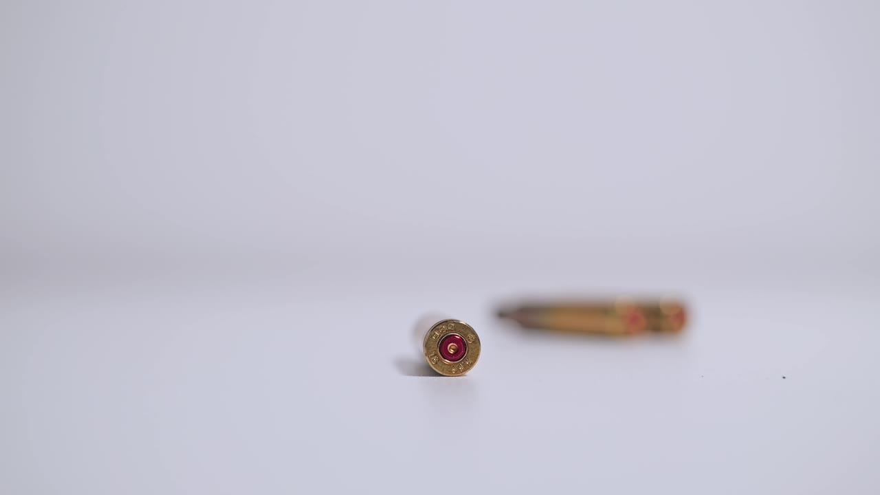 Brass bullets roll into frame beside single round on smooth white surface
