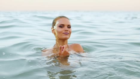 mujer atractiva sexy en el agua en la playa hace señas para seguirla y mirando a la cámara y coqueteando con el espectador