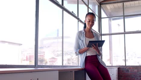 African-american-casual-businesswoman-using-tablet-by-window-in-office,-slow-motion,-copy-space