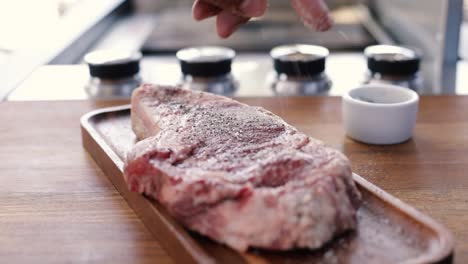 person seasoning steak with salt and pepper on cooking board stylishly