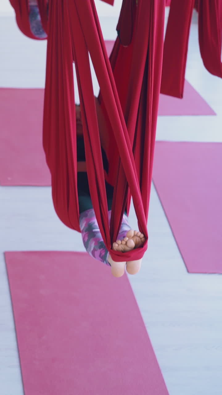 camera moves along fly yoga classroom with ladies practicing energy recovery lying in special bright red hammocks
