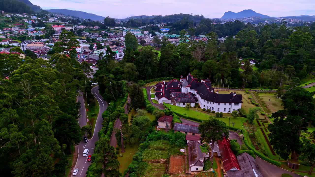 Nagranie z drona Nuwara Eliya na Sri Lance, ukazujące bujne zielone wzgórza, plantacje herbaty, budynki w stylu kolonialnym i wysokie drzewa z krętą drogą biegnącą przez miasto.