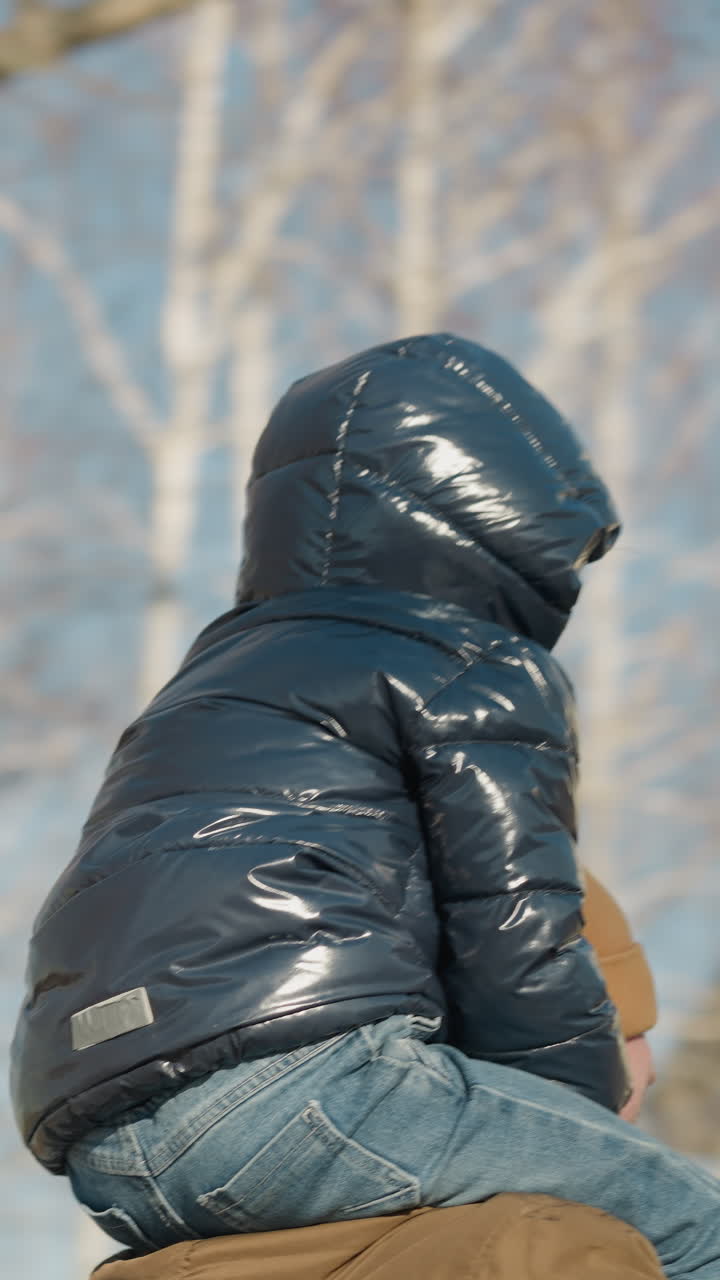 una vista rotativa de un padre llevando a su hijo en sus hombros con los ojos cubiertos con un gorro, mientras se mueven felizmente, con un poste de luz al lado