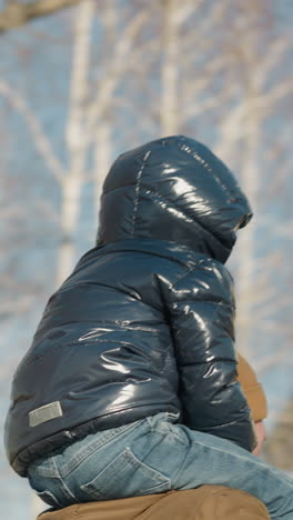 una vista rotativa de un padre llevando a su hijo en sus hombros con los ojos cubiertos con un gorro, mientras se mueven felizmente, con un poste de luz al lado