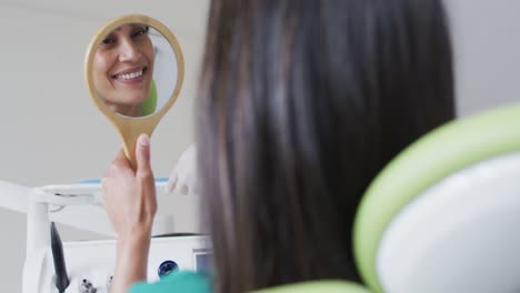 paciente de dos razas mirando sus dientes y sonriendo en el espejo en una clínica dental moderna