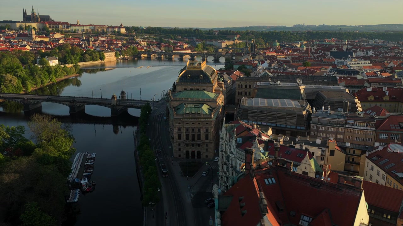 Dronekuva Kansallisteatterista Vltava-joen rannalla, Prahan linna ja Pyhän Vituksen katedraali näkyvissä joen toisella puolella lämpimässä aamuvalossa, Praha, Tšekin tasavalta.