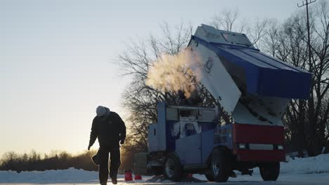 Silhouette-of-worker-walking-next-to-Zamboni-ice-resurfacer-on-frozen-lake-at-sunrise