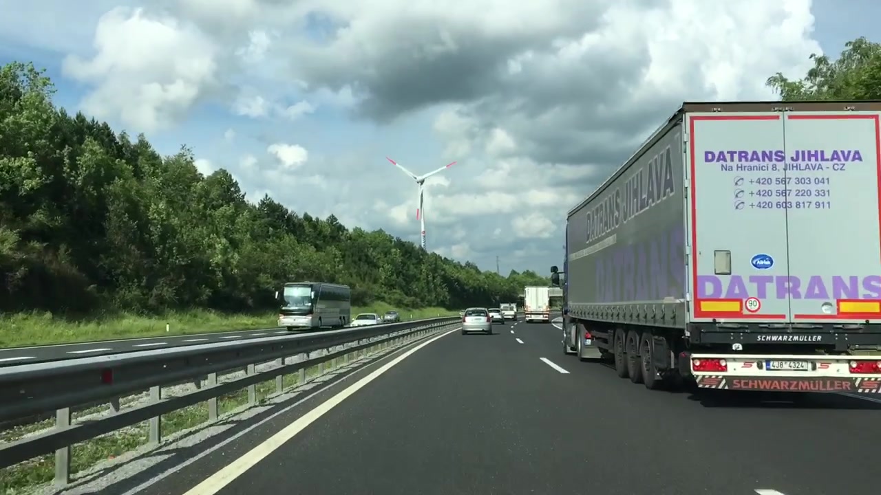 高台の道を運転中、遠くで風力タービンが回転している。
