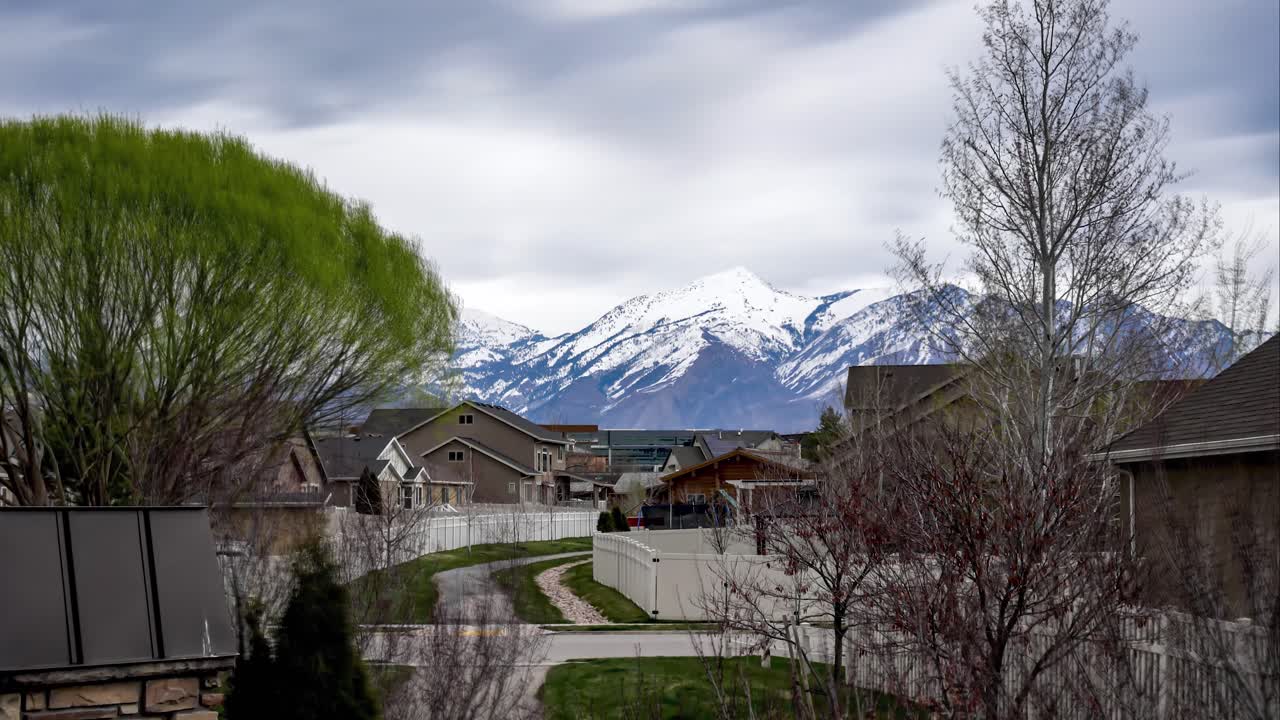 lapso de tiempo en un día nublado de un paisaje nublado que sopla sobre las montañas nevadas más allá de un suburbio de viviendas