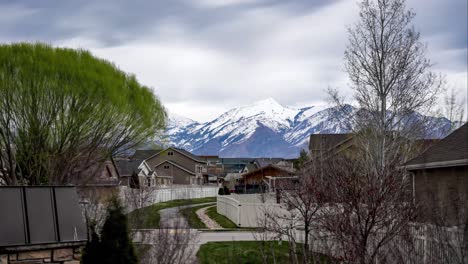 Zeitraffer-An-Einem-Bewölkten-Tag-Mit-Einer-Wolkenlandschaft,-Die-über-Die-Schneebedeckten-Berge-Hinter-Einem-Wohnvorort-Weht