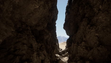 a view through a narrow canyon, with sand dunes and mountains in the distance.