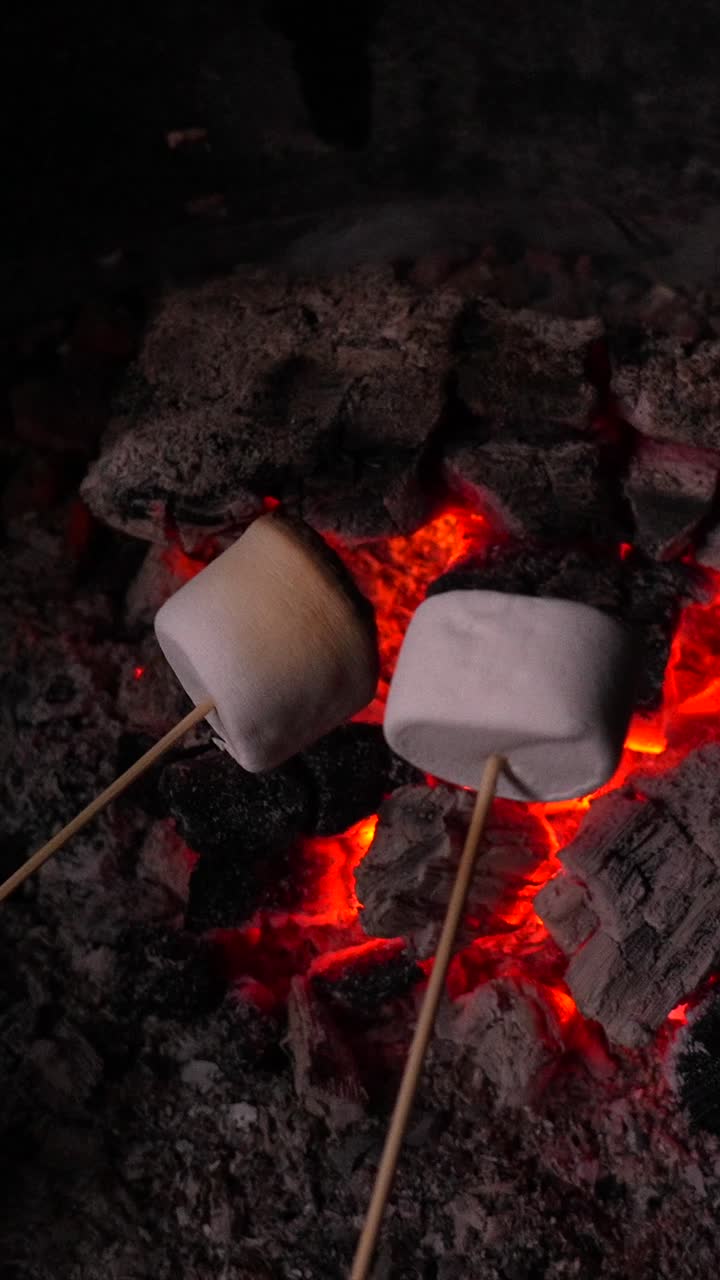 Arrostire marshmallow su braci incandescenti di un falò di notte