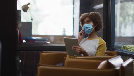 african american woman wearing face mask using digital tablet at modern office