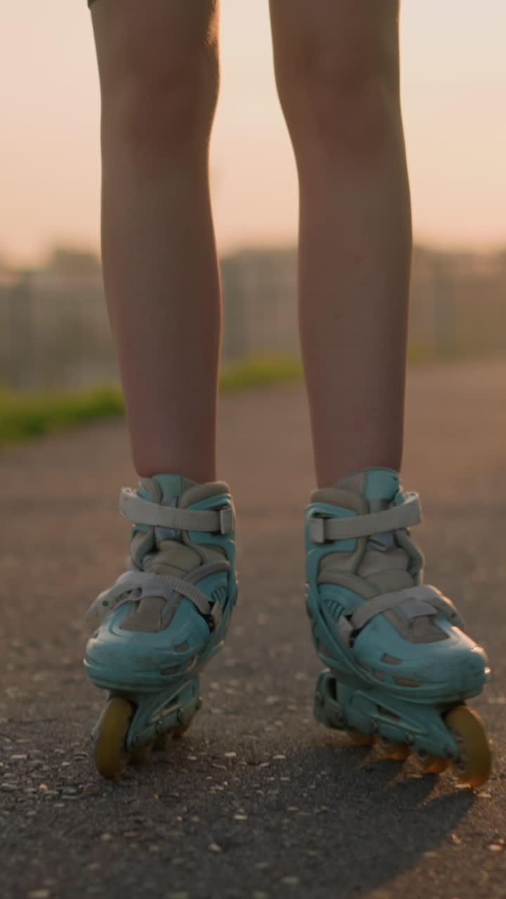 Close-up of lady's legs roller skating outdoors, with legs opening and closing as she balances on pavement during warm evening, sunlight shines from behind, casting shadows on pavement