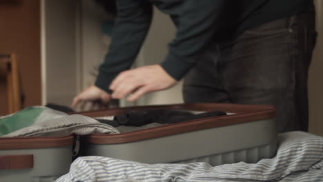 closeup, man packs clothes in grey suitcase, closes zipper, and carries away