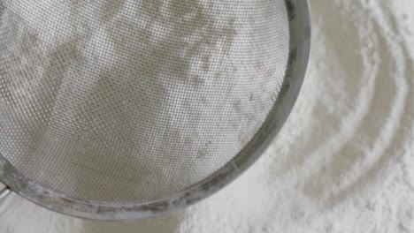 close-up of sifting flour through fine mesh sieve