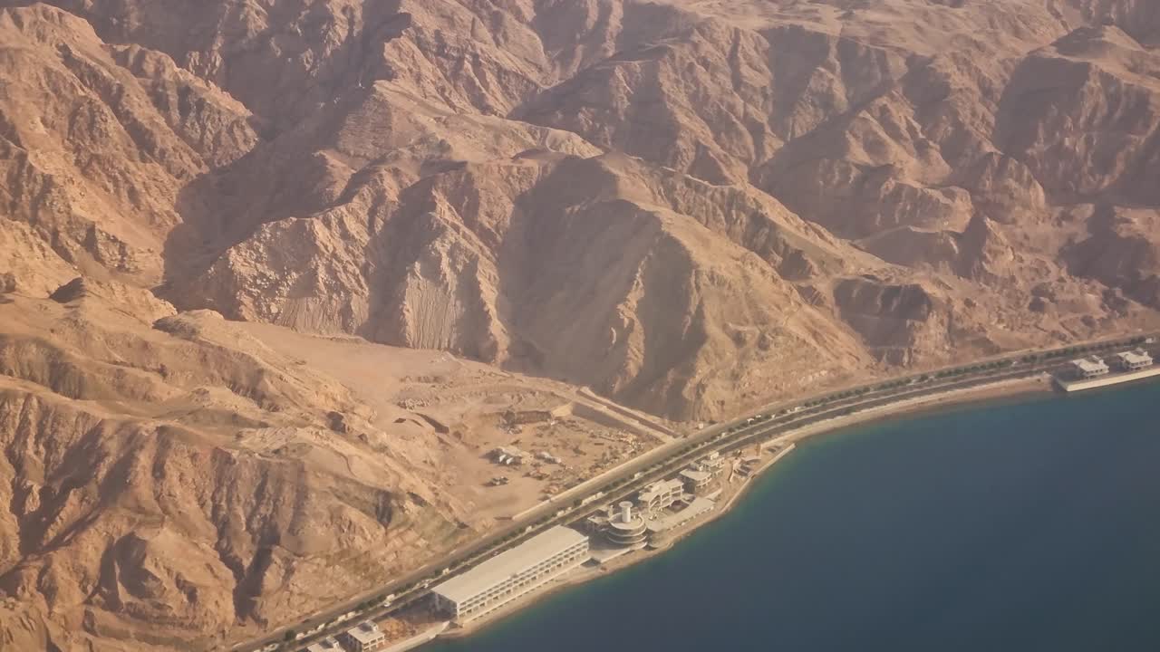 Vista da un finestrino dell'aereo su montagne desertiche e la costa del Mar Rosso, che mostra vasti paesaggi aridi, terreni accidentati e contrasti scenografici tra mare e deserto durante un volo tranquillo, Giordania.