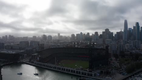 Aerial wide reverse panning shot of Oracle Park with Downtown San Francisco in the background on a foggy day