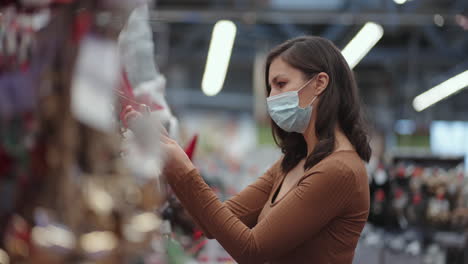 una mujer con una máscara protectora en una joyería y guirnaldas con juguetes para árboles de navidad y en casa. guirnaldas navideñas y decoración